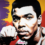 Pannello in tessuto dedicato a Muhammad Ali, con una rappresentazione dell'iconico campione che simboleggia forza, determinazione e coraggio. Un elemento decorativo che porta potenza, ispirazione e grandezza al tuo spazio.